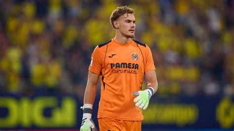 Write informative laconic excerpt under 30 words in mexican spanish for news below. Do not wrap it into quotation marks or html tags. Filip Jörgensen is set to join Chelsea from Villarreal. Photo by Fran Santiago/Getty ImagesChelsea are closing in on a €24.5million ($26.6m) deal to sign Villarreal goalkeeper Filip Jörgensen, sources have told ESPN.The 22-year-old is expected to fly to the United States -- where Chelsea are on pre-season tour -- to undergo a medical and sign a seven-year contract.Jörgensen only agreed a new long-term contract with Villarreal last month but Chelsea convinced the Denmark Under-21 international to move to Stamford Bridge, where there will now be a reshuffle in the goalkeeping positions.Djordje Petrović finished last season as first-choice goalkeeper after Robert Sánchez suffered a knee injury in December.However, Mauricio Pochettino has since been replaced as head coach by Enzo Maresca, who places greater emphasis on playing out from the back and Jörgensen is viewed as a better fit for that style, casting doubt over the futures of both Petrović and Sánchez.Petrović did not travel to the U.S. while Sánchez played the opening 45 minutes of Chelsea&apos;s first friendly, a 2-2 draw against Wrexham in Santa Clara.Chelsea also have goalkeepers Marcus Bettinelli and Lucas Bergström on their books while Kepa Arrizabalaga has also returned from a season-long loan at Real Madrid. ,El guardameta Filip Jörgensen está a punto de unirse al Chelsea desde Villarreal por €24.5 millones. Se espera que firme un contrato de siete años.