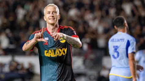 Write informative laconic excerpt under 30 words in mexican spanish for news below. Do not wrap it into quotation marks or html tags. CARSON, Calif. -- Willkommen to MLS, Marco Reus.Days after LA Galaxy head coach Greg Vanney stated that he would need "miracles" to finalize Reus&apos; documentation before the weekend, the former Germany international provided a marvel of his own after debuting in the 62nd minute of Saturday&apos;s match against Atlanta United.Backed by a vociferous sold-out home crowd of 25,174 at Dignity Health Sports Park, the 35-year-old winger made a meteoric impact that highlighted he&apos;s not just in California for a pleasant west coast vacation at the end of his career.Rapidly elevating an encounter that had struggled to catch fire, Reus was noticeably incisive with his decision-making. After providing a clever assist for Riqui Puig to open the scoring in the 76th minute, Reus then sent the stadium into a frenzy with a goal of his own in the 84th to secure a dramatic 2-0 victory."[I&apos;ll] enjoy the days, the summer and all that stuff, but ... I&apos;m not here to enjoy too much of the sun," Reus had told ESPN ahead of the game. "I&apos;m here to be successful with the team, and of course, to try to bring the Championship back to the Galaxy."With the team currently sitting on top of MLS&apos; Western Conference, dreams of snapping an agonizing 10-year title drought for the league&apos;s all-time leading champions could soon materialize. Guided by a youthful core of attacking players that have yet to reach the peak of their abilities, the Galaxy had only lost five times in its previous 26 matches of the 2024 regular season and, during that run, only two other teams in MLS surpassed its 50-goal tally.So could Reus could be the extraterrestrial game-changer that helps the Galaxy&apos;s stars align and win its first MLS Cup in a decade? You wouldn&apos;t blame optimistic fans for believing that more miracles may lie ahead: standing near the statues of Galaxy legends like Landon Donovan and David Beckham, supporter Alex Martinez told ESPN before kick-off: "It&apos;s a big signing. It&apos;s definitely going to boost the team."The evidence from Saturday&apos;s win is a clear indication of that."I have a lot of energy in my tank"Marco Reus came off the bench to grab a goal and assist vs. Atlanta and turn the game on its head. Shaun Clark/Getty ImagesReus is here to play. Yes he is another aging European superstar taking a final paycheck in MLS before retirement, but the weekend&apos;s performance showed his ambition."First of all, I want to prove myself, still," Reus told ESPN. "I&apos;m 35 years old, but I think I have a lot of energy in my tank, and of course, we want to bring the Championship home. I mean, this is the big goal for this club. Like I said, it was 10 years ago. It&apos;s a long time."Stoically analyzing the Atlanta game from the bench --- and later close to the net while warming up in front of a fan that lifted a homemade "Willkommen Reus" sign --- the German knew exactly what to do. In a tight game at 0-0, Reus entered the field and turned it into a chessboard, finding new avenues and ways to distribute and manipulate the ball up the field.When asked before the match what he believed was his best talent, the winger highlighted a trait that was on full display in his debut. "Maybe [my] vision," he said. "It&apos;s always important to think about one or two steps earlier in different situations."Galaxy general manager Will Kuntz admitted that the winger has everything you need up front. "His quality is obvious when you watch him play," he said. "I think he&apos;s got positional versatility; he&apos;s obviously got huge game experience. He&apos;s been a goal scorer, a goal creator, somebody who&apos;s dangerous on the ball."Most concerning for future opponents is that Reus wasn&apos;t fully fit against Atlanta. After the win, the veteran admitted that he was "dead [tired] after a couple of minutes," and yet, he still picked up an assist and goal without much trouble."He came in and he brought class, composure, intelligence obviously, quality, a lot of things," coach Vanney said after the game. "In a way, he made things look a little bit easy at times, where it&apos;s just smooth, in the flow and the rhythm of the game, and just picking things out."This is significant for a Galaxy side that hasn&apos;t exactly had things come easy in recent years. Saturday&apos;s party-like atmosphere and 2024 in general have been a welcome change of pace for the group that were once seen as fading giants in MLS, no longer able to keep pace with new franchises such as their crosstown rivals LAFC.The Galaxy are now title-contenders with Reus in their squad. But it&apos;s also important to note that it wasn&apos;t so long ago when they were not only struggling on the field, but also the worst team in MLS.Bouncing backMarco Reus won four trophies with Dortmund and twice finished as a Champions League runner-up. Shaun Clark/Getty ImagesTechnically speaking, 2014&apos;s MLS Cup wasn&apos;t the last trophy that the Galaxy won --- if we&apos;re counting unofficial titles. The Wooden Spoon, an award created by the Independent Supporters Council of North America (ISC), is given at the end of each season to supporters of the MLS team that finishes at the bottom of the overall standings."This is a trophy that no one wants, and it should be that way," ISC President Jeremy Wright said in 2016.With a paltry total of eight wins from 34 matches in the 2017 season, and a dead-last position in MLS&apos; standings, supporters of the Galaxy were sent the Wooden Spoon. For an organization that proudly boasts itself to be the most successful in MLS, 2017 was a year to forget and the 8W-18L-8D record was cemented as its lowest in franchise.Dan Thomas is joined by Craig Burley, Shaka Hislop and others to bring you the latest highlights and debate the biggest storylines. Stream on ESPN+ (U.S. only). Rene Trejo, a long-time supporter from East L.A. who was grilling at the parking lot tailgate with his family before Saturday&apos;s game, grimaced when discussing the 2017 season with ESPN. "You go through those moments and you&apos;re like [exasperated sigh], another loss, another bad season," he said. "It felt rough."Regardless of the long list of high-profile transfers added -- like Gio dos Santos, Ashley Cole, Zlatan Ibrahimovic, Javier "Chicharito" Hernandez and Douglas Costa -- the Galaxy strategy prioritized headline-grabbing stars over on-field substance.What followed was a playoff absence in five of its last seven seasons. The team lacked cohesion and chemistry and from 2017-2023 the Galaxy was the second-worst team in MLS for goals allowed in the regular season, with 399 let in through 223 games (via TruMedia/StatsPerform). Through that period, it failed to claim a victory in 145 matches, meaning that 65% of its regular season games ended without a win.Along with poor results that had the Galaxy rotating through a handful of coaches, within their higher ups, there was legitimate roster mismanagement that led to a fine of $1 million in late 2022. By early 2023, boiling point was reached through a boycott from supporters that eventually led to the firing of president Chris Klein."Yeah, last season was definitely a rough, rough one," Jose, a Galaxy fan from Westminster at Saturday&apos;s tailgate who was eating with friends, told ESPN. "But as time goes on, you just got to hope for the best."Things look much different in 2024.Coupled with bringing Kuntz into the front office, the Galaxy shifted to look for more low-key but highly effective signings ahead of the current season. That has meant doing plenty of homework, but the inclusion of younger faces such as Gabriel Pec and Joseph Paintsil has found an attacking harmony with other up-and-coming figures such as roaming midfielder Puig and goal-scoring striker Dejan Joveljic.And while the signing of Reus seems to be a return to old ways, what&apos;s different now is that he won&apos;t be the singular focus like many previous stars. Reus, despite his otherworldly magic on Saturday, is happy to be another piece of the Galaxy puzzle.playWhy MLS is a &apos;good option&apos; for Marco ReusJulien Laurens and Gab Marcotti discuss Marco Reus&apos; links to St. Louis City.Helping wake "a sleeping giant"Instead of basking in the glory of his impressive debut, Reus, clearly a team player, was blunt in Saturday&apos;s post-match news conference about his preference for assisting over scoring. "I mean, I&apos;m an offensive player, so that [scoring] is always my target to help the team, but it&apos;s not my first choice," he said. "Most of the time I like to give assists to my teammates."That statement is a testament to the new type of player the Galaxy are aiming for. Gone are the days of the egocentric Ibrahimovic, someone who referred to himself in the third person after scoring in his own Galaxy debut, declaring in 2018: "I gave them Zlatan."Granted, it may not be fair to compare the hunger of a goal scorer and the penchant of wanting to support as a wide midfielder, but Reus seems genuine in his desire to be an equal part of Galaxy&apos;s group. Regardless of being in his mid-30s, he doesn&apos;t want the lessons to be a one-way street either."I&apos;m here to help my teammates to [get] better every, every single day," he added. "But of course, to learn from my team as well, from my coaching staff, and to bring new energy into this team.During the limited time he&apos;s had training with the squad, it&apos;s apparent that the veteran has already quickly helped tighten things up."In training, we feel more intense and more concentration, which is very good," Galaxy defender Maya Yoshida told the media before Saturday&apos;s game. "Sometimes we are too casual, for example, conceding the two set-pieces last week against Seattle, that&apos;s the kind of things we need to improve. He [Reus] can lift all the levels up to the next level."If you read between the lines, there&apos;s a recognition that he may also be a rotational figure and not a go-to starter. Whether it be due to his age, his occasional injuries, or the fact that the Galaxy were actually doing quite well before he arrived, Reus might sometimes be a bench option like he was on Saturday. But that&apos;s OK."At this point in the year, nobody&apos;s feeling 100%," Kuntz told ESPN. "It [Reus&apos; arrival] allows us to maybe make some substitutions in games, whether that&apos;s Marco coming in or Marco coming off, it lets the group stay kind of maximally fresh as we come down the stretch run, and then gives us a whole bunch of different weapons, the ability to change how we want to set up from game to game or even half to half."The good news for Galaxy fans who are eager to confine the dark days of the recent past to history is that Reus has already shown he can support the Galaxy through a cameo role if needed. In just a small window of time, the visionary winger created moments out of nothing against Atlanta, completely turning the game on its head. If one is allowed to call a recent UEFA Champions League finalist a "secret weapon," that may be appropriate in this sense."It&apos;s been a long time, I think, too long since we lifted a trophy here. That is something that we really want to do, and we think Marco can be an ultimate piece for us," Kuntz said. "My conversation with Marco was like: &apos;Look, essentially you can come here and wake a sleeping giant.&apos;"Doing so would require some more miracle moments, but Reus will always make sure to highlight the fellow pieces of the puzzle around him. "I&apos;m here to bring the Championship home," he said. "And together, of course. Together with my teammates." ,El ex internacional alemán Marco Reus debuta en la MLS con LA Galaxy, impactando con un gol y una asistencia en su primer partido contra Atlanta United.