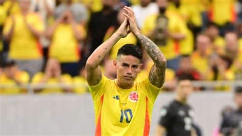 Write informative laconic excerpt under 30 words in mexican spanish for news below. Do not wrap it into quotation marks or html tags. playHerculez Gomez: James Rodriguez is the best player in the tournament (2:00)Herculez Gomez, Kasey Keller and Ali Krieger offer high praise for James Rodriguez after Colombia&apos;s huge quarterfinal win over Panama. (2:00)James Rodríguez could be set for a return to Madrid, with Rayo Vallecano eager to sign the free-agent Colombia midfielder, sources told ESPN.The LaLiga club, based in the Vallecas neighbourhood of Madrid, have been working for weeks on adding the player of the tournament at this summer&apos;s Copa América, whom they consider the ideal star to fire up the fan base for their centenary celebrations, sources said.Sources also indicated that Rodríguez, who played for Real Madrid from 2014-20, would welcome a return to the city and has given his blessing to a deal with Vallecano, even at a reduced salary.One obstacle to the move is LaLiga&apos;s economic control requirements. Vallecano have discreetly been working on making the numbers work, but the situation has been difficult to resolve at this late point in the transfer period, sources added.A source close to the player told ESPN that a deal with Vallecano is in its final stages, though the club has denied this is the case.Rodríguez played last season with São Paulo but did not sign a new contract to remain with the Brazilian club. In a nomadic career since leaving Madrid, he has also played for Bayern Munich on loan, Everton, Al Rayyan and Olympiacos.Rodríguez starred at the recent Copa América in the United States, contributing a tournament-record six assists as his team reached the final before losing to Argentina. ,Rayo Vallecano busca fichar al mediocampista colombiano James Rodríguez, ex Real Madrid y figura de la Copa América, para celebrar su centenario.